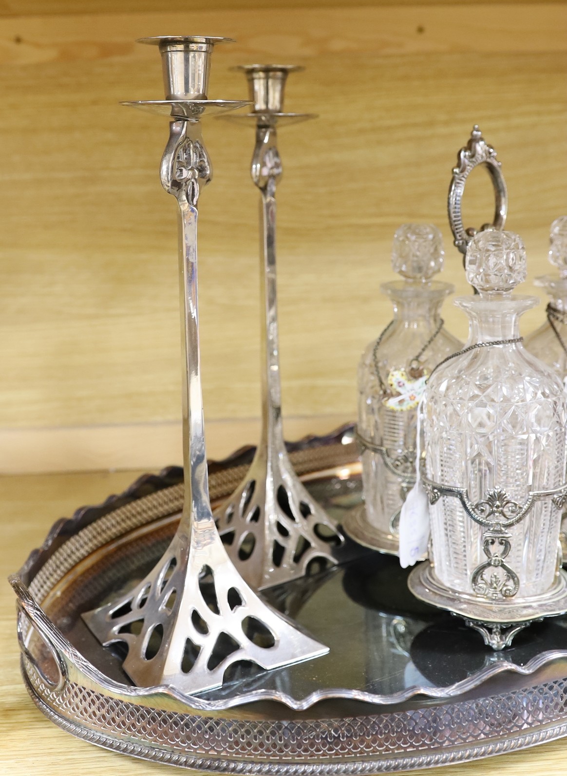 An oval silver plated tray, a three bottled tantalus and a pair of candlesticks, a silver ‘Whiskey’ label, two enamelled silver labels ‘Gin’ and ‘Whisky’ and two plated labels